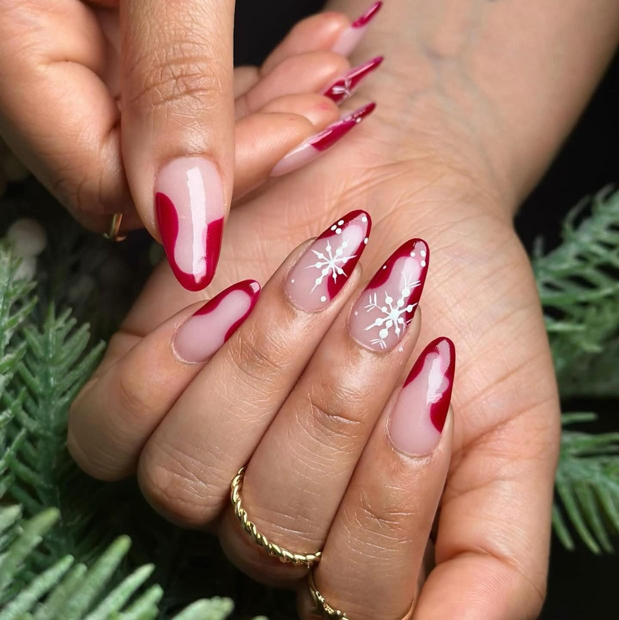 Almond nude nails with red accents and white snowflake designs
